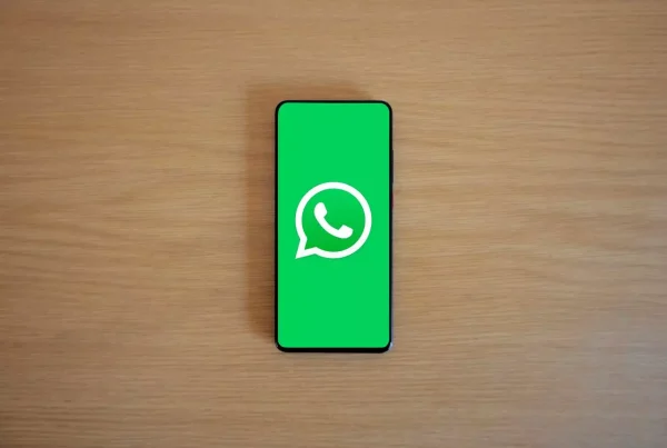 foto de un celular sobre una mesa de madera. El celular tiene un solo color de fondo verde con el logo de whatsapp centrado